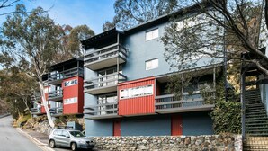 Un edificio residencial de varios pisos con balcones, un muro de piedra en la fachada y un automóvil estacionado.