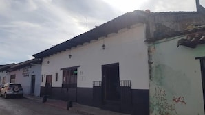 Un edificio de fachada blanca, puerta negra y un pequeño balcón. Hay un cartel sobre la puerta y un coche estacionado al frente.