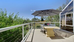 Ein Balkon mit Tisch und Stühlen, einem Sonnenschirm und Blick auf Grünflächen und Hügel.
