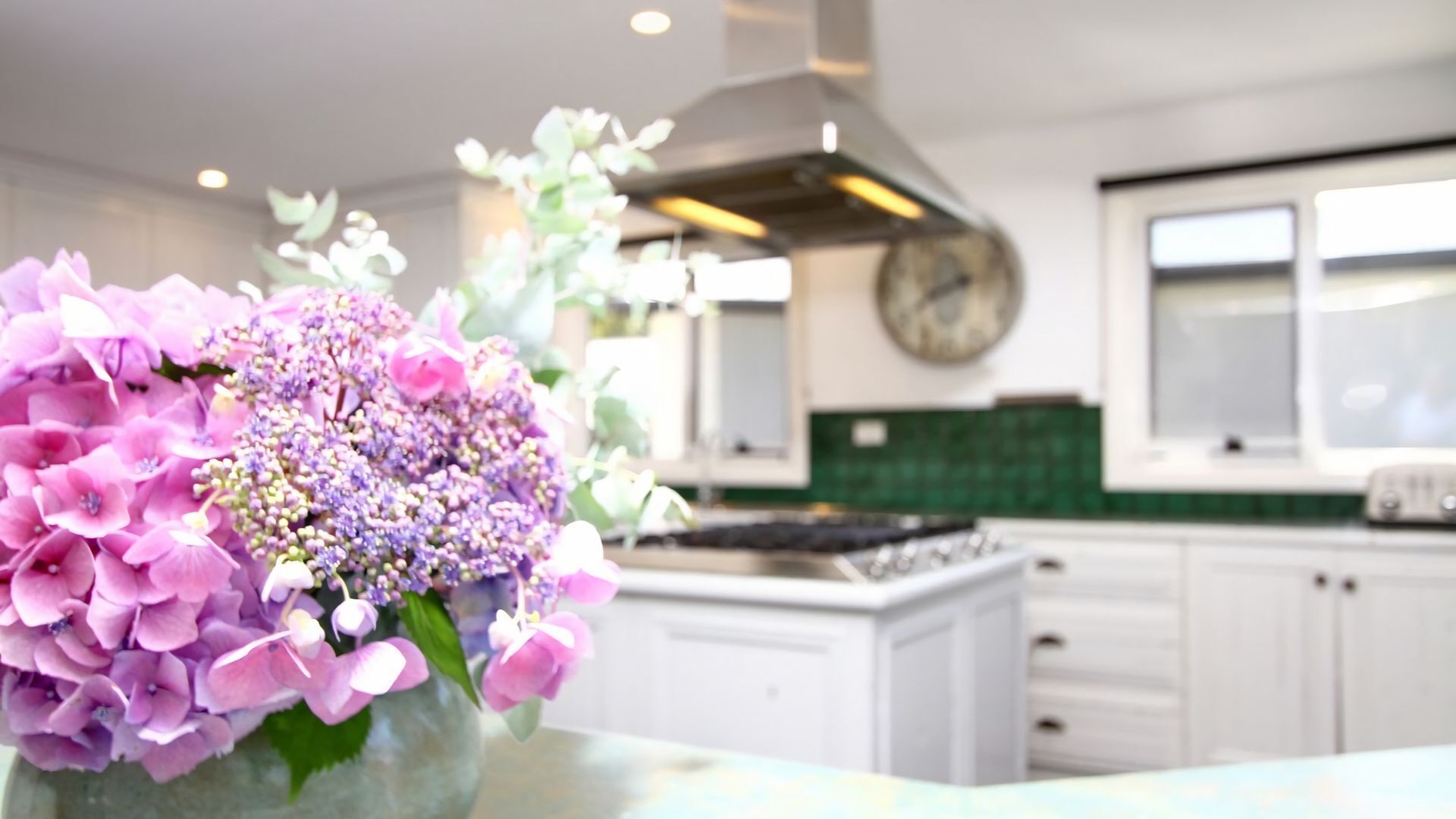 A modern kitchen with white cabinets, a stainless steel range hood, and a green backsplash.