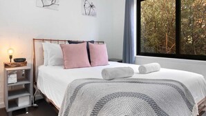 A neatly made bed with pillows, a bedside lamp, and a view of trees through a window. - Aspen Court 8 is a comfortable and spacious apartment (Jindabyne)