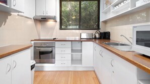 A modern kitchen with white cabinetry, a built-in oven, a microwave, and a window with blinds. - Aspen Court 8 is a comfortable and spacious apartment (Jindabyne)