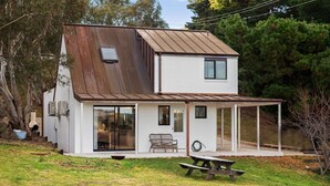 Ein zweigeschossiges Haus mit Metalldach, großen Glasfenstern und einer überdachten Terrasse.