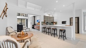 A modern kitchen with a central island, bar stools, and a dining area with a round table and chairs. - The Jindabread House, true alpine experience in modern comfort. (Jindabyne)