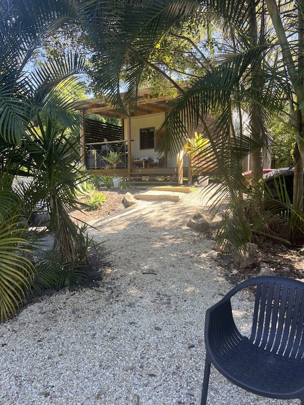 A gravel pathway leading to a wooden structure with a covered seating area, surrounded by palm trees. - Three Rivers Getaway Cabin (Yandina)