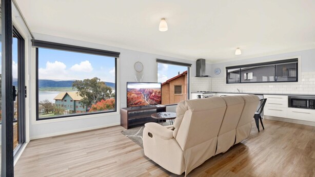 Una sala moderna con un ventanal grande, un sofá, televisor y una zona de cocina.