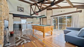 A spacious living area with a pool table, a sofa, and a kitchen in the background. - Old Hut Creek Chalet with a peaceful rural outlook (Jindabyne)