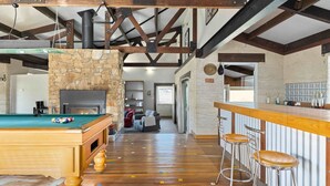 A cozy bar area with a pool table, a stone fireplace, and a bar stool. - Old Hut Creek Chalet with a peaceful rural outlook (Jindabyne)
