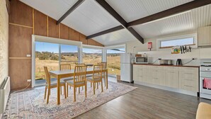 A modern kitchen with a large window, wooden dining table, and a view of the countryside. - Old Hut Creek Chalet with a peaceful rural outlook (Jindabyne)