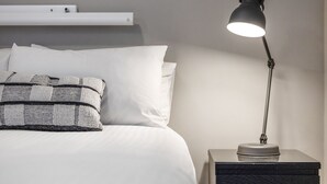 A neatly made bed with white linens and a patterned throw blanket. There is a bedside table with a lamp and a small, dark-colored box. - Horizons 307, resting on the shores of Lake Jindabyne (Jindabyne)