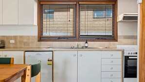 Eine kleine Küche mit Geschirrspüler, Backofen und einem Fenster mit Jalousien.