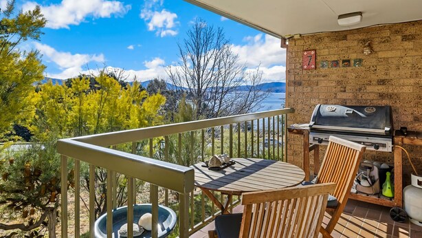 Ein Balkon mit Blick auf Berge und Bäume, inklusive Grill und Tisch mit Stühlen.