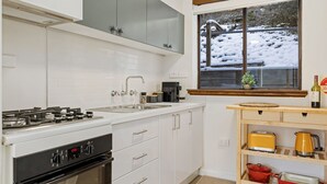 Uma cozinha moderna com armários brancos, fogão a gás, pia e janela com vista para uma paisagem coberta de neve.