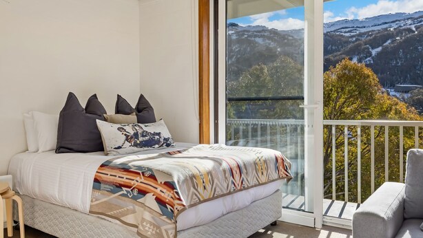 Quarto com cama, almofadas e vista para uma paisagem montanhosa através de uma grande janela.