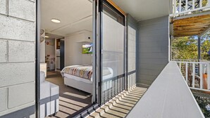 Uma varanda com guarda-corpo de madeira, uma cama com colcha estampada e vista para o exterior.