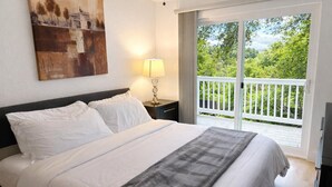 Hotellihuone, jossa on sänky, yöpöytä, lamppu ja liukuovellinen lasiterassi, josta avautuu näkymä vehreään maisemaan.