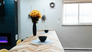 Un comedor moderno con una mesa de madera, dos cuencos negros, un florero con flores amarillas y una chimenea.