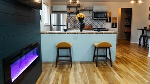 Una cocina moderna con una isla central, taburetes de bar, una parrilla empotrada e iluminación colgante.
