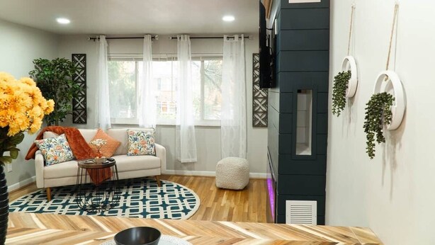 Una sala de estar con un sofá, una mesa de centro, un tapete estampado y un televisor montado en la pared.
