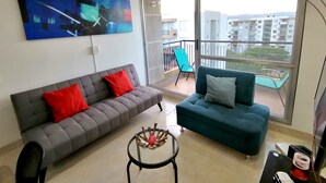 A modern living room with a grey sofa, a teal sofa, and a glass coffee table. - Confortable Apartamento Vacacional  (Ricaurte)