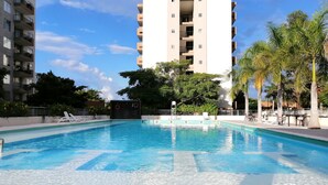 A swimming pool with clear blue water, surrounded by lounge chairs and palm trees. - Confortable Apartamento Vacacional  (Ricaurte)