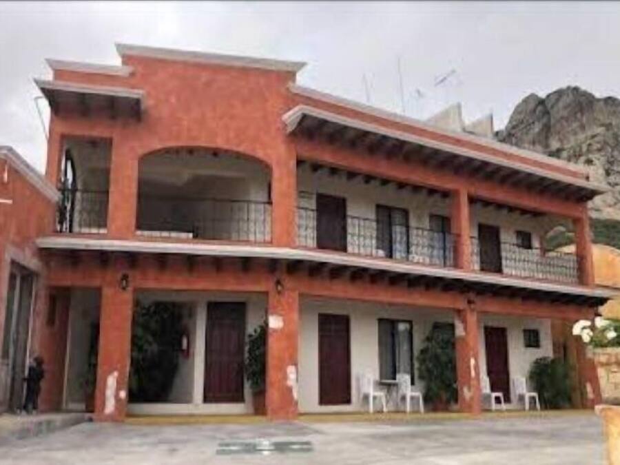 A two-story building with a red facade, multiple balconies, and a mountain in the background.