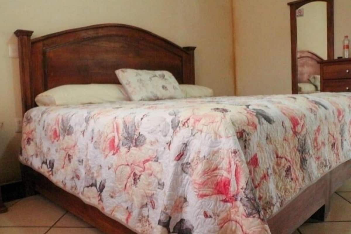 A bedroom with a wooden bed frame, floral bedding, and a nightstand.