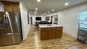 A modern kitchen with wooden cabinets, a stainless steel refrigerator, a marble island, and a dining area with a TV. - Come and enjoy a family stay in a beatiful Lake House. (Lake Placid)