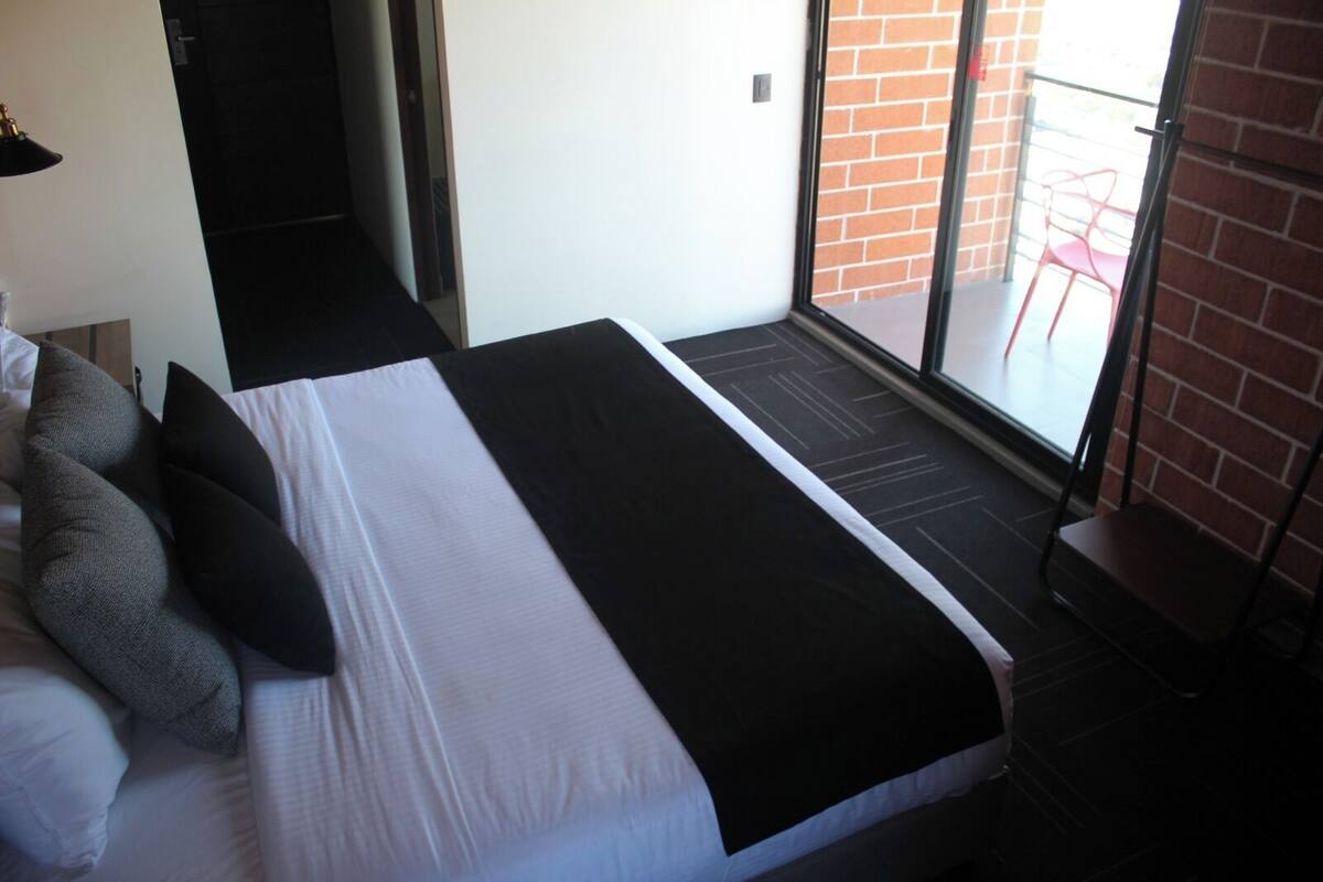A hotel room with a large bed, a small desk, a chair, and a view of the outside.