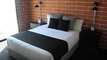 A neatly made bed with a black and white bedspread, two black lamps on nightstands, and a brick wall background.