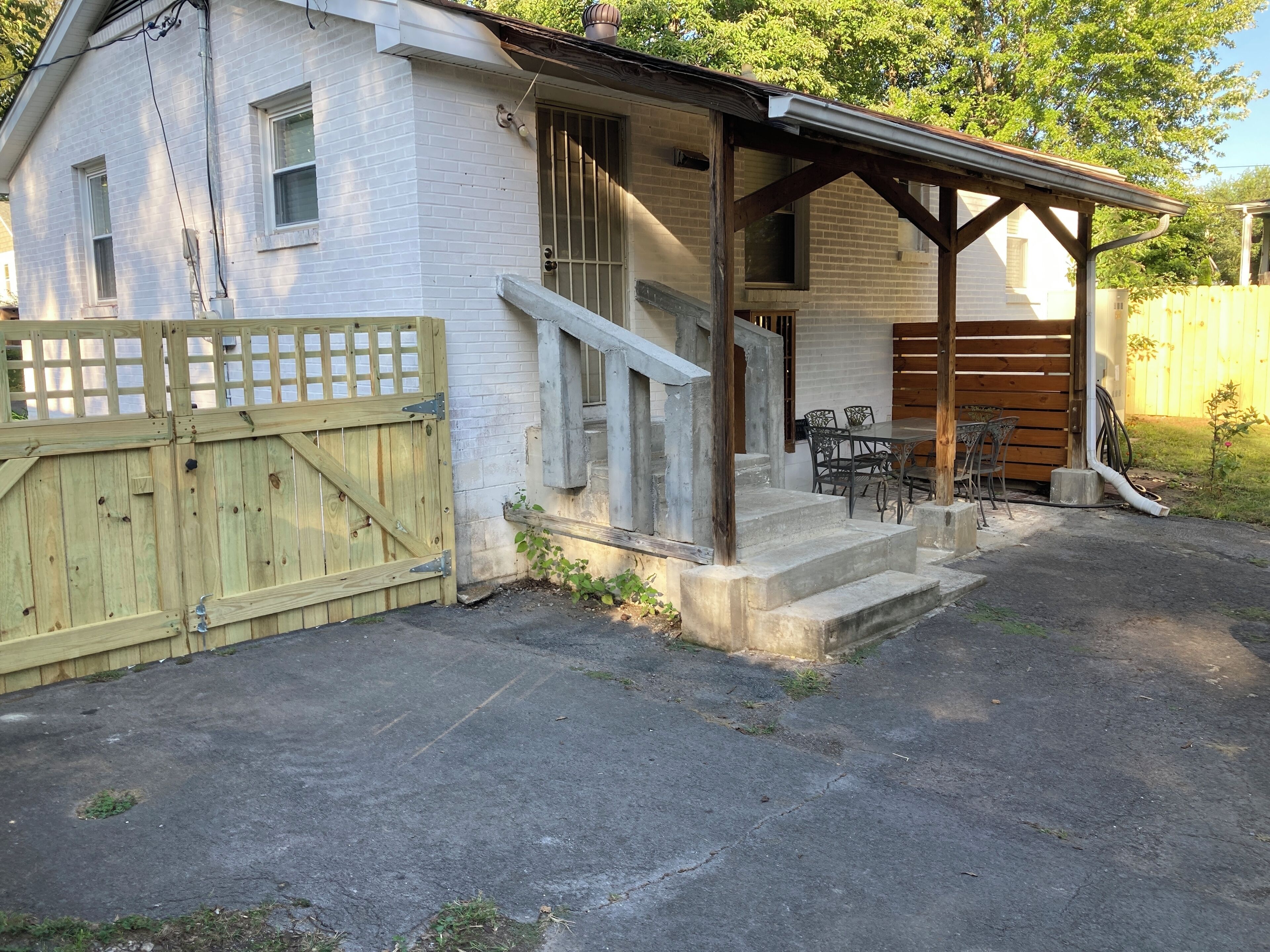 A white brick building with a wooden gate, a covered porch, and a table with chairs outside.