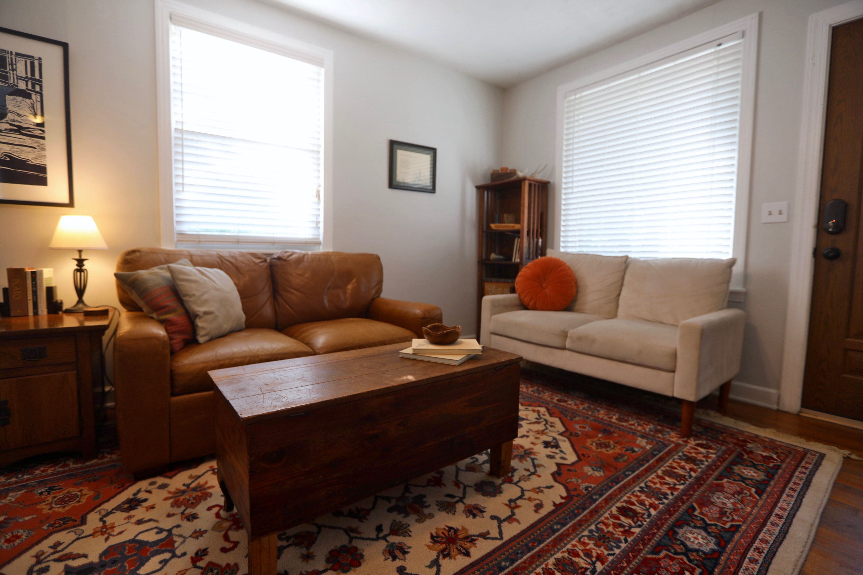 A living room with a brown leather sofa, a white sofa, a wooden coffee table, and a patterned rug.