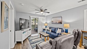 A spacious living room with a ceiling fan, a television, a blue sofa, a coffee table, and a leather chair.