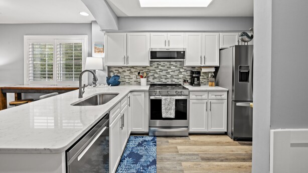 A modern kitchen with white cabinets, stainless steel appliances, and a blue patterned rug.