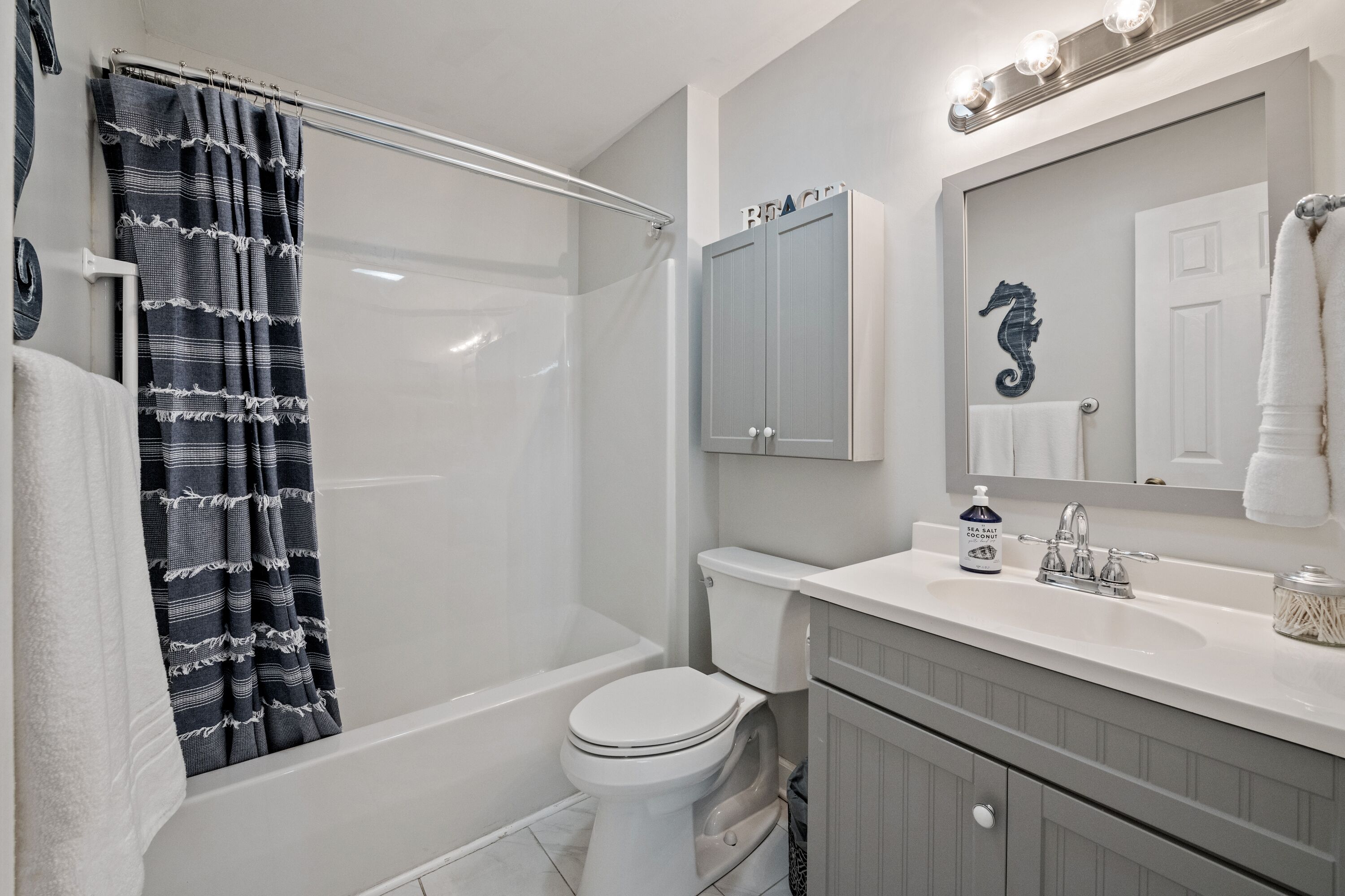 A bathroom with a bathtub, toilet, vanity, and a mirror with lights above.