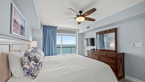 A bedroom with a bed, a ceiling fan, a dresser, a TV, and a window with curtains. - Oceanfront 3BD/3BA at Bluewater Keyes (806) (North Myrtle Beach)