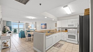 A modern kitchen with white cabinets, a central island, and a view to the living area. - Oceanfront 3BD/3BA at Bluewater Keyes (806) (North Myrtle Beach)