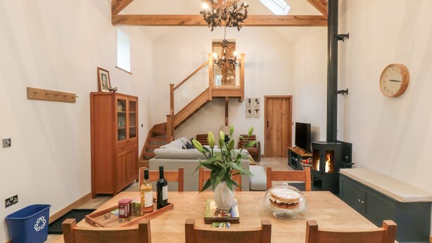 Un salon chaleureux avec une table à manger en bois, des chaises, un lustre, une cheminée et un escalier menant à l’étage supérieur.