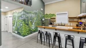 Une cuisine moderne dotée d’un bar, d’une fresque représentant une forêt et d’un escalier menant à un niveau supérieur.