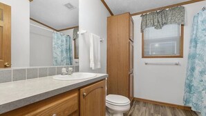 A compact bathroom with a wooden vanity, a white sink, and a toilet. - Wolf River Cabin B - Fremont, WI (Fremont)
