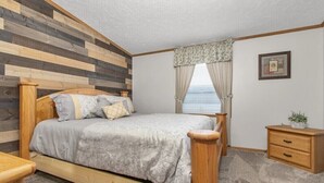 A bedroom with a wooden bed, a nightstand, a small drawer unit, and a window with curtains. - Wolf River Cabin B - Fremont, WI (Fremont)