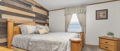 Quarto com cama de madeira, mesa de cabeceira, gaveteiro e janela com cortinas.