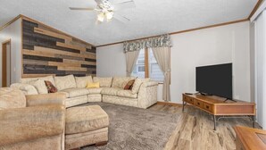 A living room with a sectional sofa, a flat-screen TV, a ceiling fan, and a wooden accent wall. - Wolf River Cabin B - Fremont, WI (Fremont)