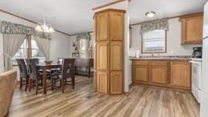 A compact kitchen with wooden cabinets, a dining area with chairs, and a chandelier. - Wolf River Cabin B - Fremont, WI (Fremont)