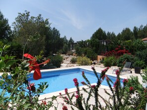 A swimming pool surrounded by lush greenery and red flowers, with steps leading up to a building in the background. - Villa Lorena Avec Grande Piscine Privée, au Calme et a 3 km de la mer (L'Ametlla de Mar)