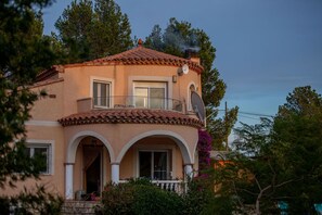 A two-story house with a tiled roof, a balcony, and a chimney emitting smoke. - Villa Lorena Avec Grande Piscine Privée, au Calme et a 3 km de la mer (L'Ametlla de Mar)