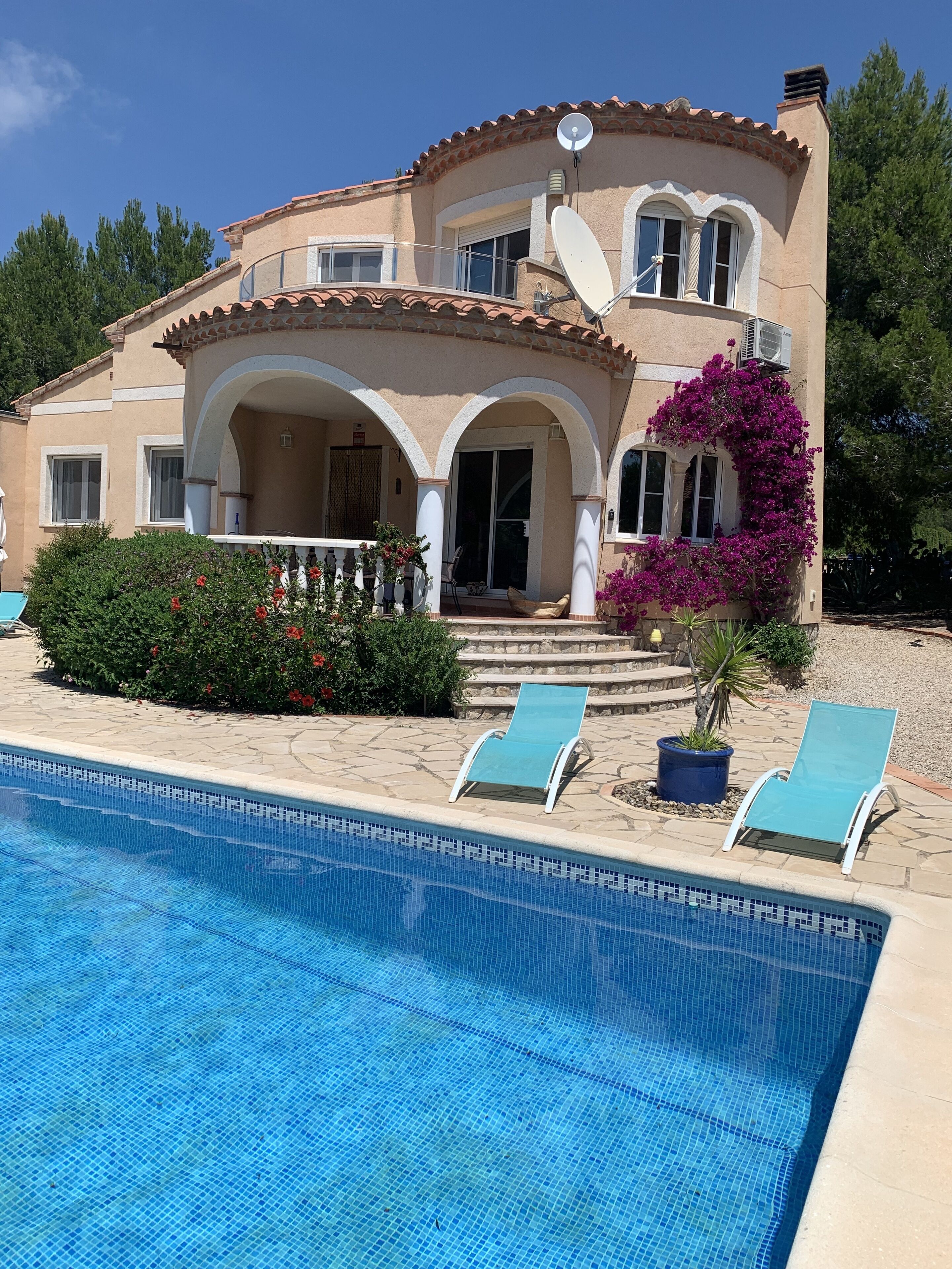 A two-story house with a swimming pool, outdoor seating, and satellite dishes.