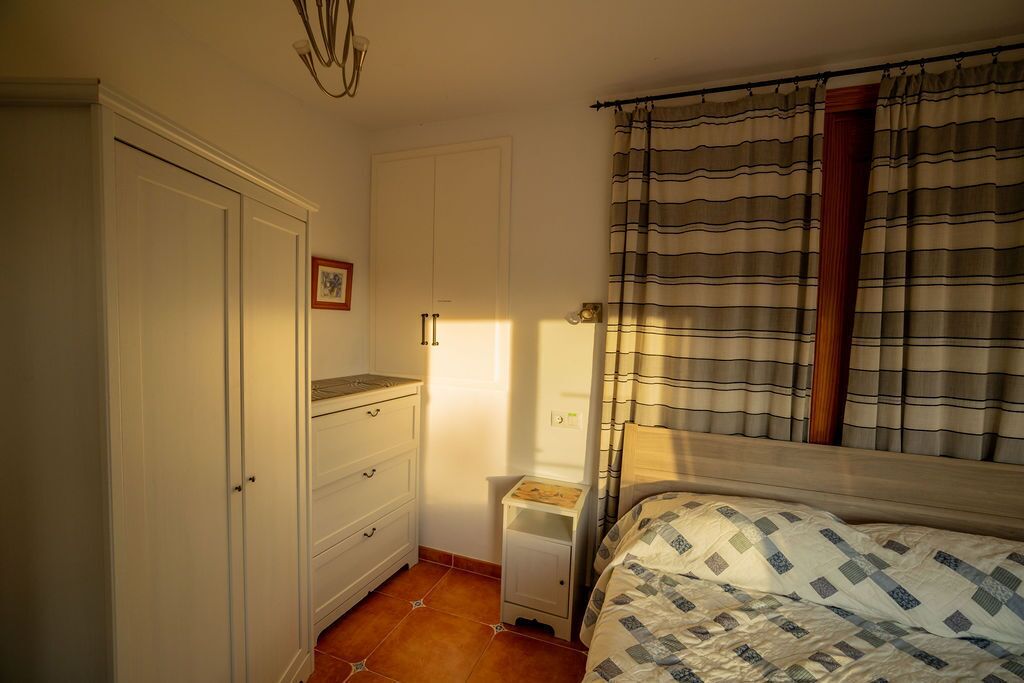 Une chambre à coucher avec un lit, une table de chevet, une armoire et une fenêtre avec des rideaux.