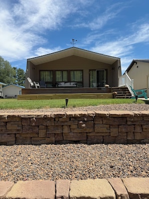 A single-story house with a porch, a stone wall in the foreground, and a clear sky.