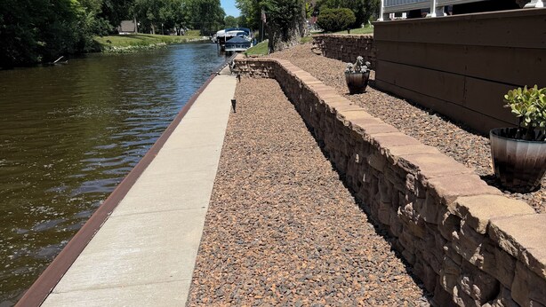 A riverbank walkway with a stone wall, a concrete path, and a white fence. - Relax with Nature (Coldwater)